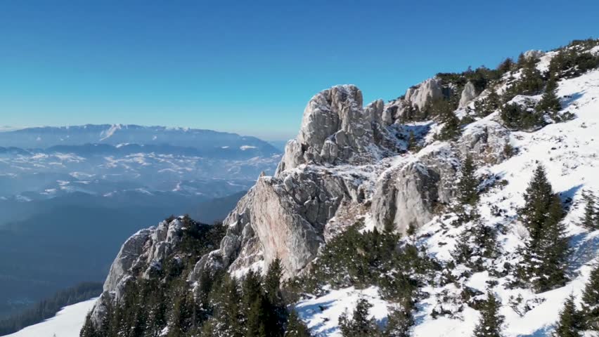 A drone view of the snowy peaks of the Bucegi Mountains of Romania with the Piatra Craiului ridge in the background on a sunny day