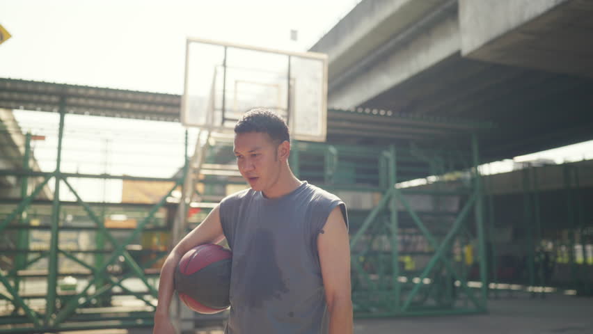 Wellness outdoor sport training street basketball. Asian Sportsman basketball player drinking water from a bottle after sport fitness workout exercise playing streetball at outdoor court in the city.
