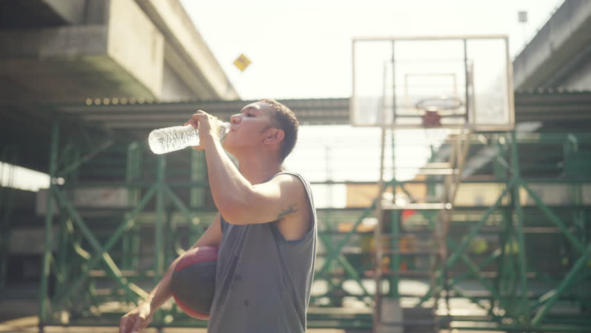 Wellness outdoor sport training street basketball. Asian Sportsman basketball player drinking water from a bottle after sport fitness workout exercise playing streetball at outdoor court in the city.