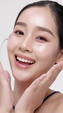 Vertical footage beautiful young Asian woman with healthy facial skin isolated over white background for skincare commercial product advertising. Slow motion shot.
