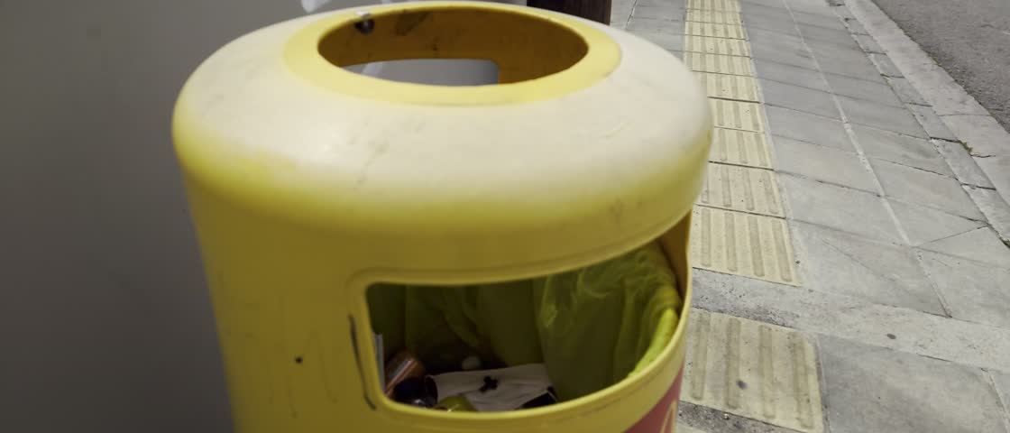 Colorful bin on urban street collects waste near pedestrian pathway in a busy neighborhood