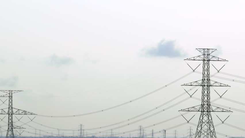 An aerial view highlights the height of the power transmission tower, with multiple lines stretching across the open sky, symbolizing the backbone of the electrical grid.
