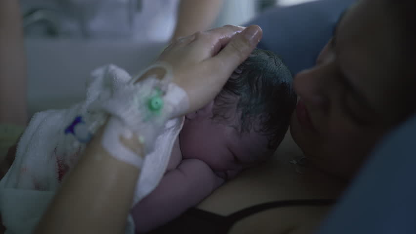 An authentic and intimate portrayal of a newborn's first seconds in life, resting against the mother's skin immediately following birth, waiting for baby to cry