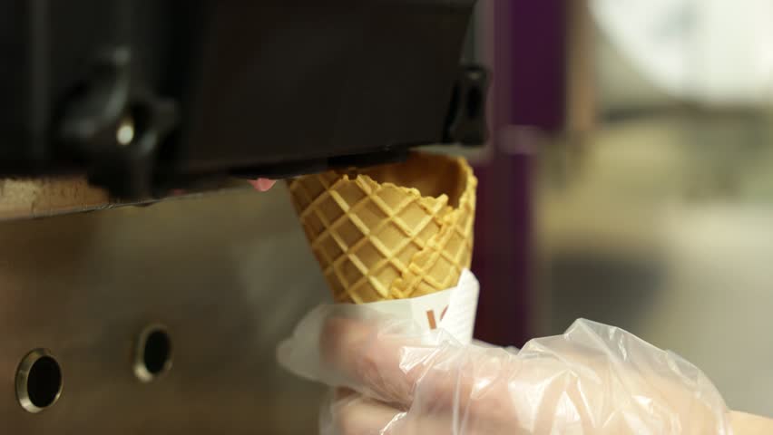 Ice cream cone being filled from a machine. ice cream from a vending machine