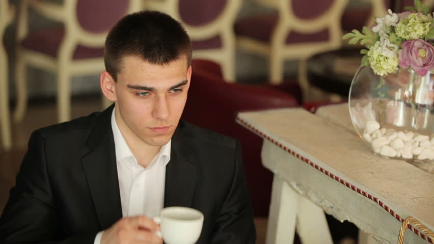 Young adult drinking coffee in a cafe and looking at camera
