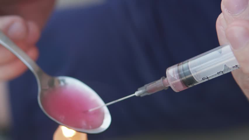 A drug addict cooks heroin on a spoon with the help of a candle fire. Drug addiction and homelessness concept.