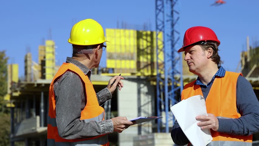 Construction Engineer and Supervisor Discussing Building Construction Near Formwork with Tower Crane. Their conversation underscores the importance of collaboration in construction projects.