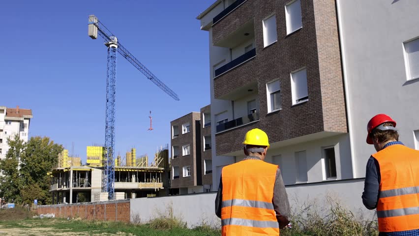 Construction Engineers Discussing New Building Project at Construction Site. A site engineer and construction supervisor are seen walking outside the construction site of a new apartment building.