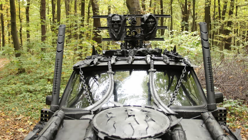 Forest setting, front view, heavy armor. Front view showing armored vehicle decorated with skulls and chains, set in wooded area, evokes dark, dystopian vibe.