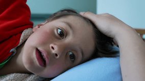 Tender moment of a young boy in a red hoodie lying down with a curious expression, as his mother gives him a gentle head massage, highlighting care, relaxation, and family bonding - Powered by Shutterstock - Get 15% off with code: PIKWIZARD15