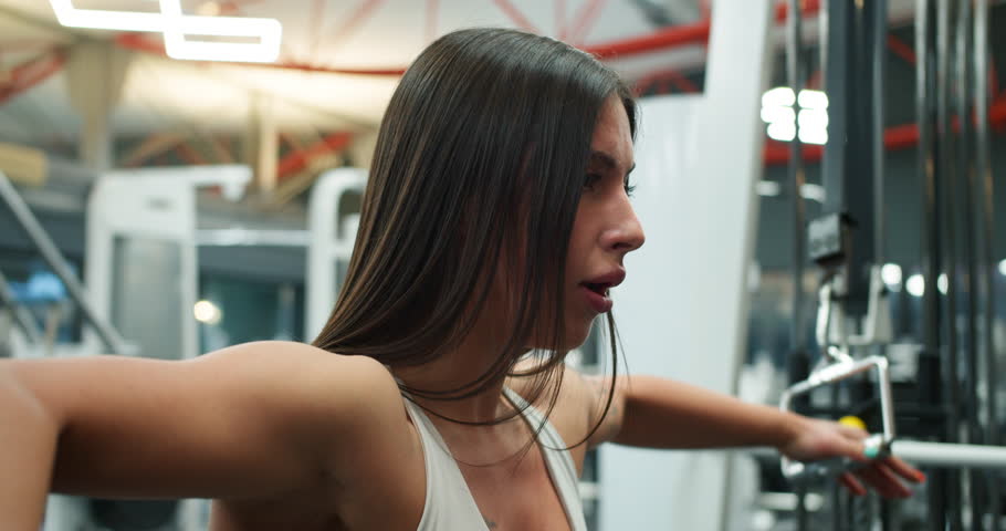 Close up of sporty girl in a white top exercises using a block trainer with ropes during her workout in the gym