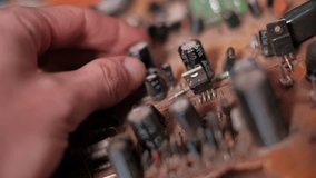 Close-up shot of fingers examining dusty electronic components, including capacitors and resistors, on an old brown printed circuit board. Electronics inspection and maintenance concept. - Powered by Shutterstock - Get 15% off with code: PIKWIZARD15