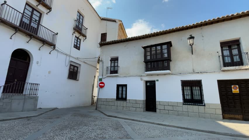 Slow-motion footage of a town square in Toledo. We see two-story whitewashed houses with balconies. We see the beautiful pebble ground; there