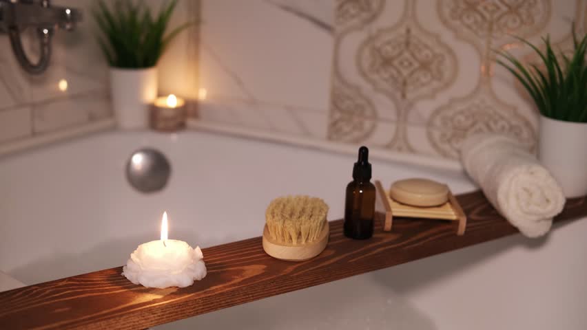 Bathroom has wooden bathtub tray with candle and bath accessories, as well as body care products. Atmosphere of relaxation. Home spa.