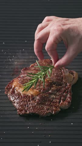 cook put fresh rosemary on grilled beef steak slice on hot electric grill surface