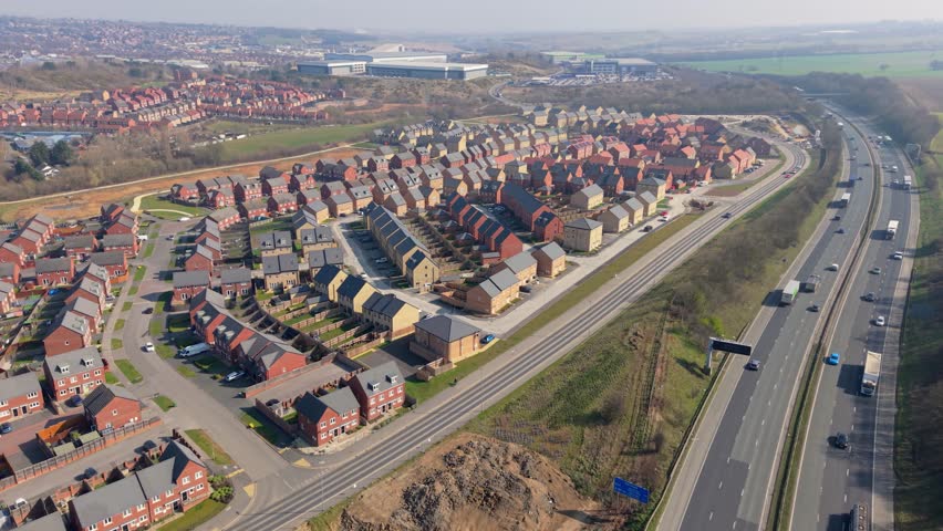 4K aerial footage of a new build housing estate on the edge of a UK city having been built on green belt land representing housing shortage and urban sprawl with transport links via motorway