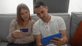 Couple using tablet on a comfortable living room sofa for online shopping with credit card, emphasizing relationship and indoor lifestyle. - Powered by Shutterstock - Get 15% off with code: PIKWIZARD15