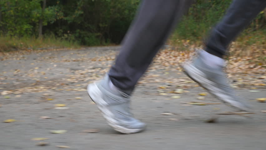 Male feet of sporty man running along road near forest at early autumn. Legs of young athlete sprinting fast along trail at nature. Strong guy jogging outdoor. Healthy active lifestyle. Low view