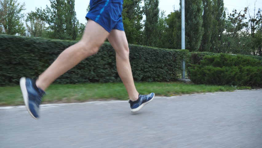 Close up male feet of sporty man running along sidewalk at summer day. Legs of young athlete sprinting fast along path at nature. Strong sportsman jogging outdoor. Healthy active lifestyle. Low view
