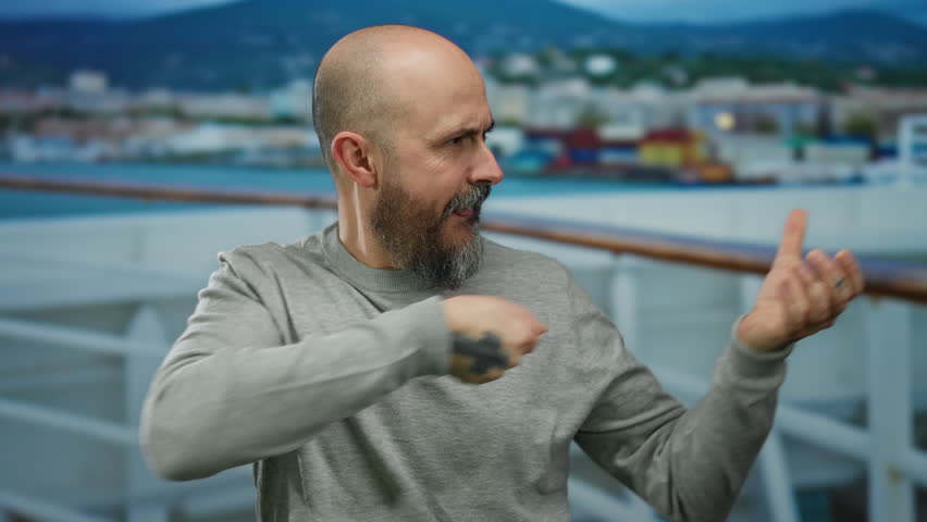 Man with beard on cruise boat pulls invisible rope against seaside backdrop.