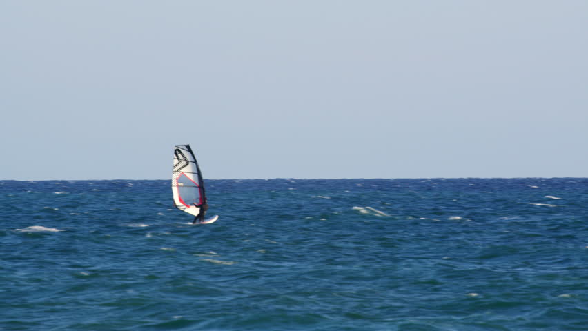 Professional windsurfer riding challenging waves, demonstrating exceptional skill and dynamic performance under bright sunny sky during thrilling water sport session