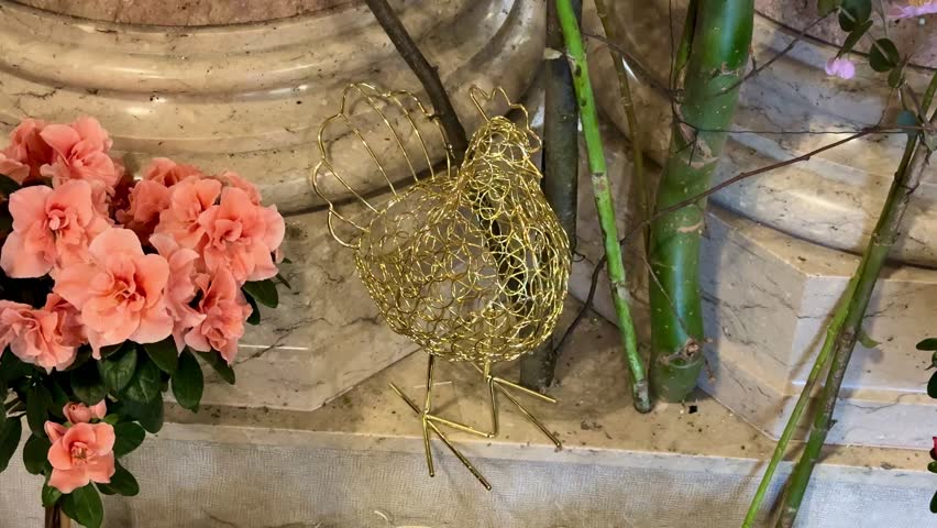 A crafted wire chicken ornament among vibrant flowers, showcasing creativity and charm in its design