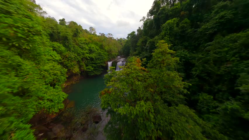 Cinematic FPV drone flight over tropical waterfall and river in lush green jungle in Thailand.