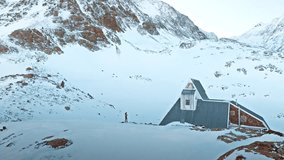 A lone figure walks through deep snow in the Pyrenees Mountains, near a quaint cabin surrounded by towering peaks and a clear winter sky. - Powered by Shutterstock - Get 15% off with code: PIKWIZARD15