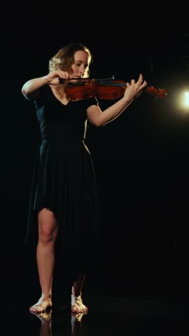 Amazing concert of classical music, female musician playing violin in darkness. Contemporary art performance on stage, vertical video, enjoy beautiful sounds of viola, talented and inspired violinist