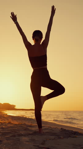Silhouette for slender woman practicing yoga on ocean beach in morning or evening, vertical shot, back view. Healthy lifestyle and sport activity, lady traveling in islands for recovery vitality