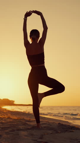 Silhouette for slender woman practicing yoga on ocean beach in morning or evening, vertical shot, back view. Healthy lifestyle and sport activity, lady traveling in islands for recovery vitality