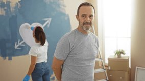 Middle-aged hispanic couple painting new home living room together with love, man smiling and woman painting heart on wall, showing family bonding and renovation process indoors. - Powered by Shutterstock - Get 15% off with code: PIKWIZARD15