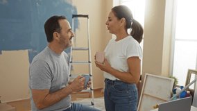 Hispanic couple enjoying a coffee break in a newly painted living room, surrounded by painting supplies and a ladder, sharing a moment of love and togetherness in their home. - Powered by Shutterstock - Get 15% off with code: PIKWIZARD15