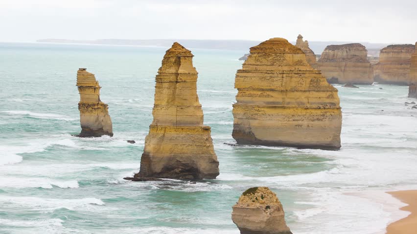 Aerial view of the Twelve Apostles rock formations with waves crashing against them under overcast skies at Port Campbell, Australia