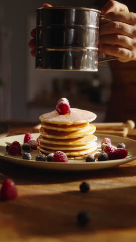 Stack of tantalizing pancakes generously sprinkled with powdered sugar. Cozy morning in beautiful kitchen illuminated by warm sunlight. Advertising vertical video. Breakfast aesthetics, culinary blog.