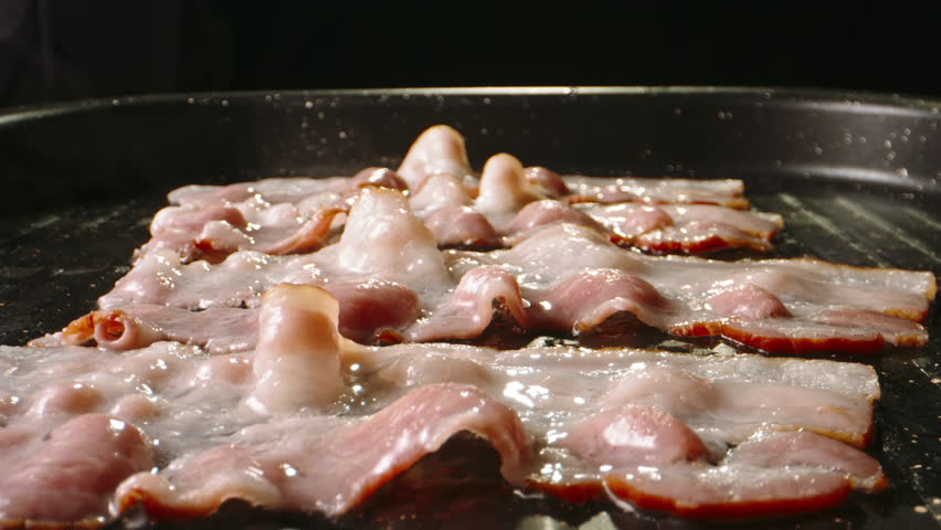 Frying halal beef bacon in pan side view close up slow motion. Crispy pieces of delicious bacon fried in hot skillet. Pan-fried bacon for mouthwatering breakfast irresistible flavor. Cholesterol