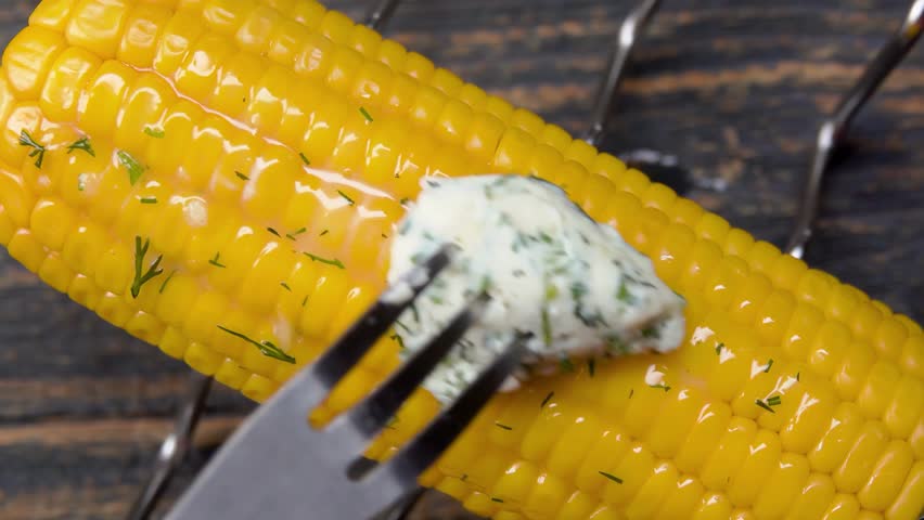 A piece of garlic butter, containing creamy butter, dill, garlic, salt, and mustard, is placed on top of freshly boiled corn on the cob. The butter begins to melt and spread over the warm corn kernels - Powered by Shutterstock - Get 15% off with code: PIKWIZARD15