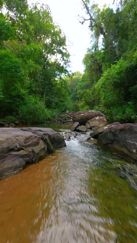 Smooth FPV drone flight over shallow tropical river with rocks in lush green jungle in Thailand