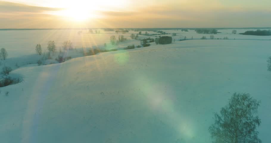 Drone aerial view of cold winter landscape arctic field, trees covered with frost snow, ice river and sun rays over horizon. Extreme low temperature weather. Siberia