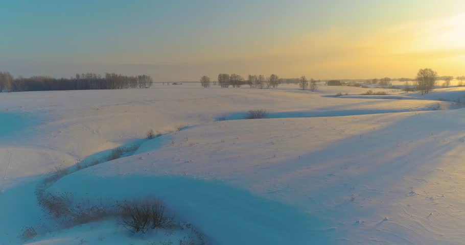 Drone aerial view of cold winter landscape arctic field, trees covered with frost snow, ice river and sun rays over horizon. Extreme low temperature weather. Siberia