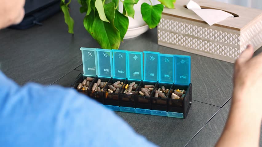 Man sorting his pills and supplements into a weekly pill organizer. Concept of medication management and daily health routine. High quality 4k footage