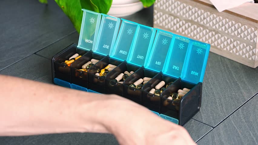 Man sorting his pills and supplements into a weekly pill organizer. Concept of medication management and daily health routine. High quality 4k footage