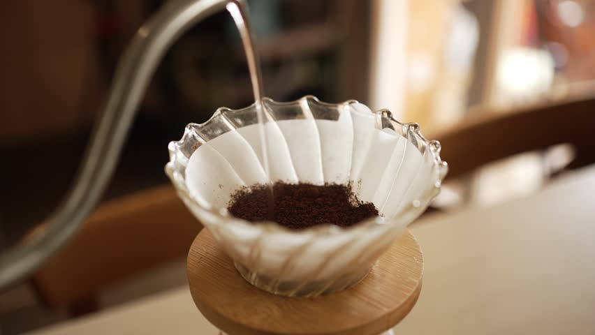 Preparation of filter coffee using the pour-over method with a v60 dripper, hot water is poured over ground coffee beans placed on a paper filter, extracting the coffee's flavor and aroma