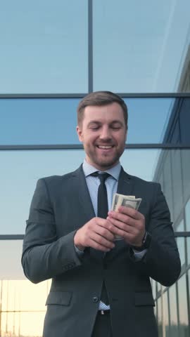 A successful businessman is seen counting cash outside his modern and sleek office space