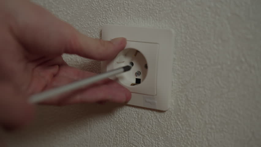 Electrician carefully using screwdriver into electrical outlet, performing essential repair and maintenance work, ensuring safety and functionality, close-up. Shooting in slow motion.