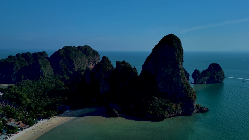 Witness breathtaking views of towering limestone cliffs rising from the turquoise sea in southern Thailand. This stunning coastal landscape showcases pristine beaches and lush greenery in Krabi