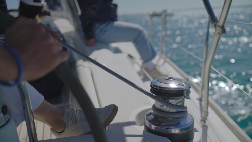 Sailboat crew performs a tack maneuver, shifting from sunlight to shadows while managing ropes on deck.