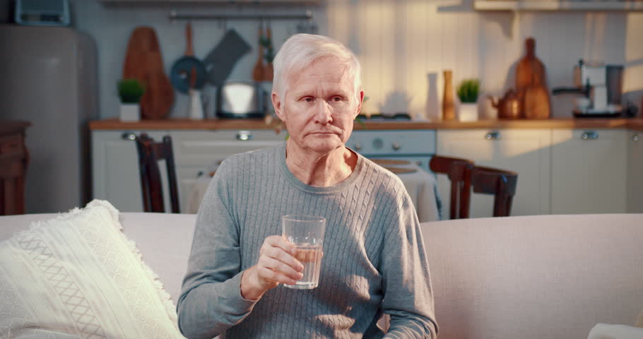 Elderly man drinking water from glass at home, healthy lifestyle, body hydration . Portrait of aged male person in living room, healthy nutrition and diet for lose weight, curing disease by hungry