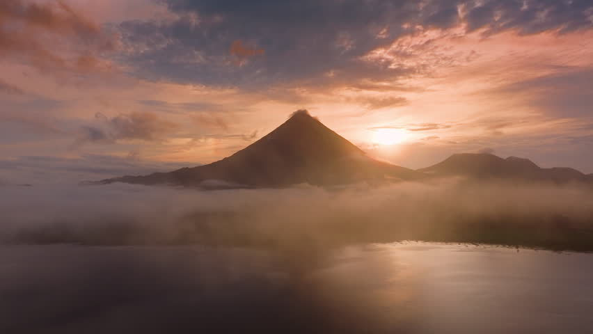 Experience stunning aerial views of the sunrise over Laguna de Arenal and Volcan Arenal in Costa Rica, surrounded by mist and greenery, creating a tranquil paradise for nature lovers