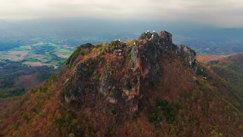Aerial approach of mountaintop temples at Wat Chaloem Phra Kiat surrounded by dramatic cloudy sky